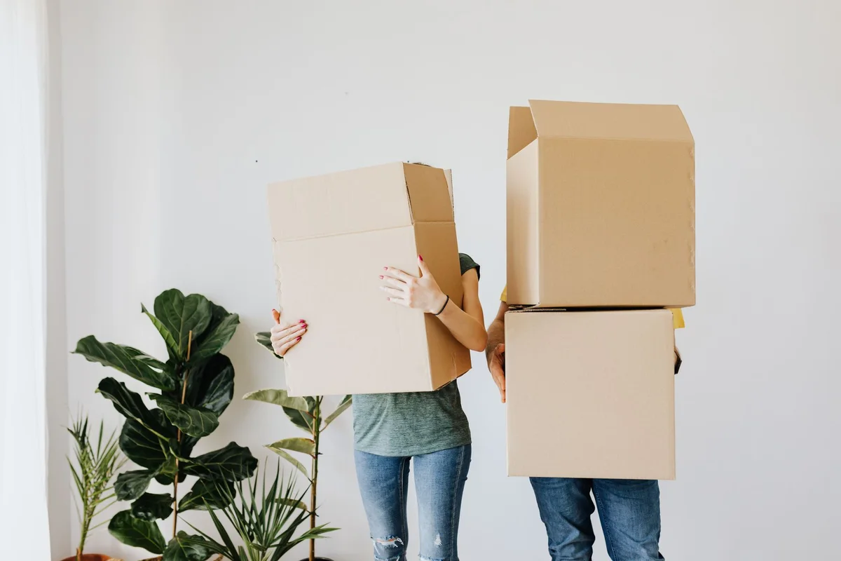 People carrying moving boxes into a home; illustrative stock photography, not a Broom Home listing.
